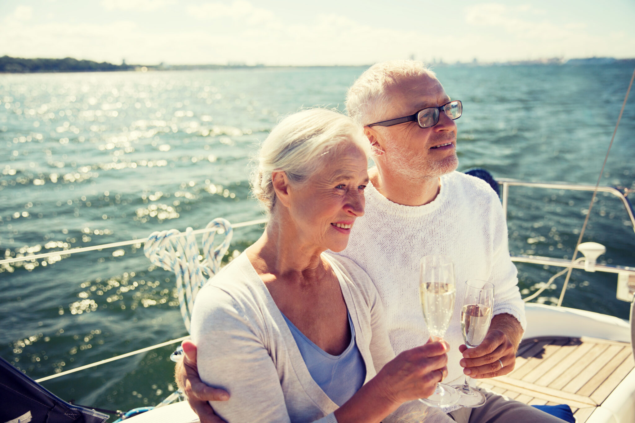 sailing, age, tourism, travel and people concept - happy senior couple drinking champagne on sail boat or yacht deck floating in sea